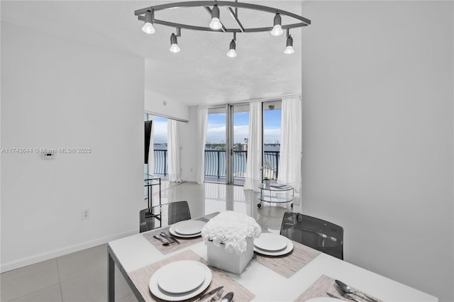 tiled dining space with a wall of windows, baseboards, a water view, and rail lighting