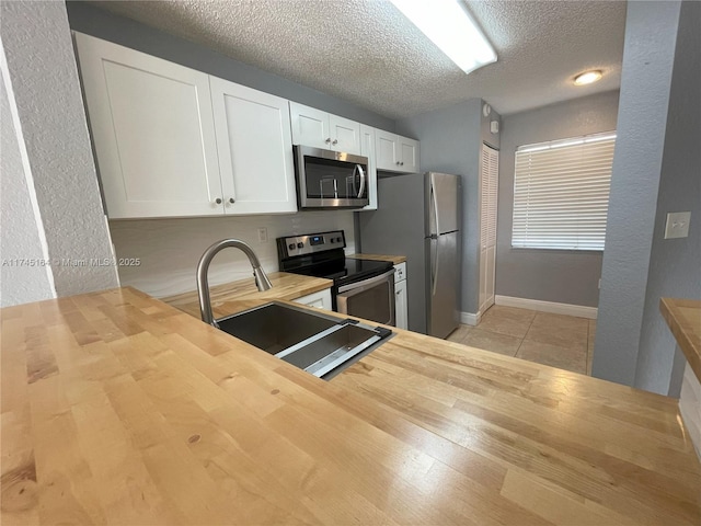 kitchen featuring wood counters, appliances with stainless steel finishes, sink, white cabinetry, and a textured ceiling