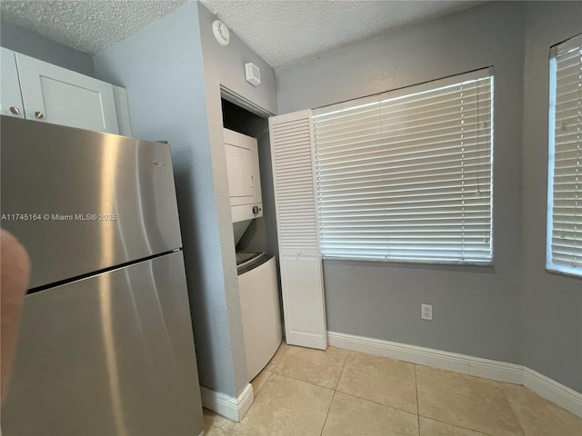 kitchen featuring light tile patterned floors, white cabinetry, a textured ceiling, stainless steel refrigerator, and stacked washer and dryer