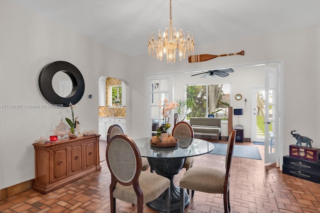 dining area featuring brick floor, arched walkways, and ceiling fan with notable chandelier