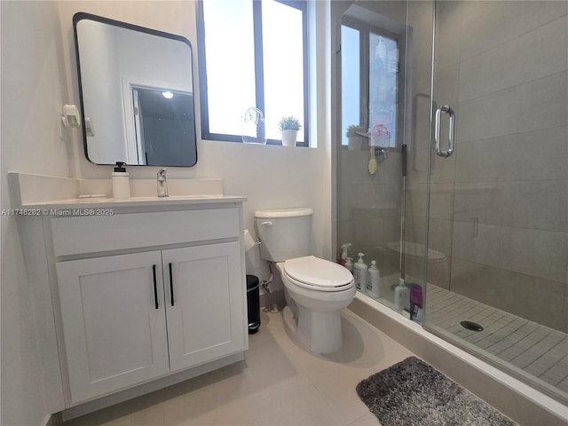 bathroom featuring toilet, vanity, tile patterned flooring, and a shower with shower door