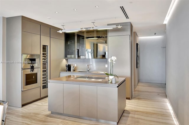 kitchen with a center island with sink, stainless steel double oven, gray cabinetry, sink, and black stovetop