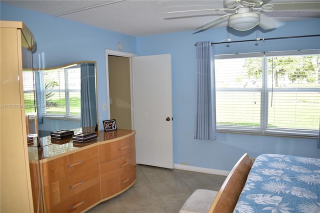 bedroom with ceiling fan, baseboards, a textured ceiling, and light tile patterned flooring