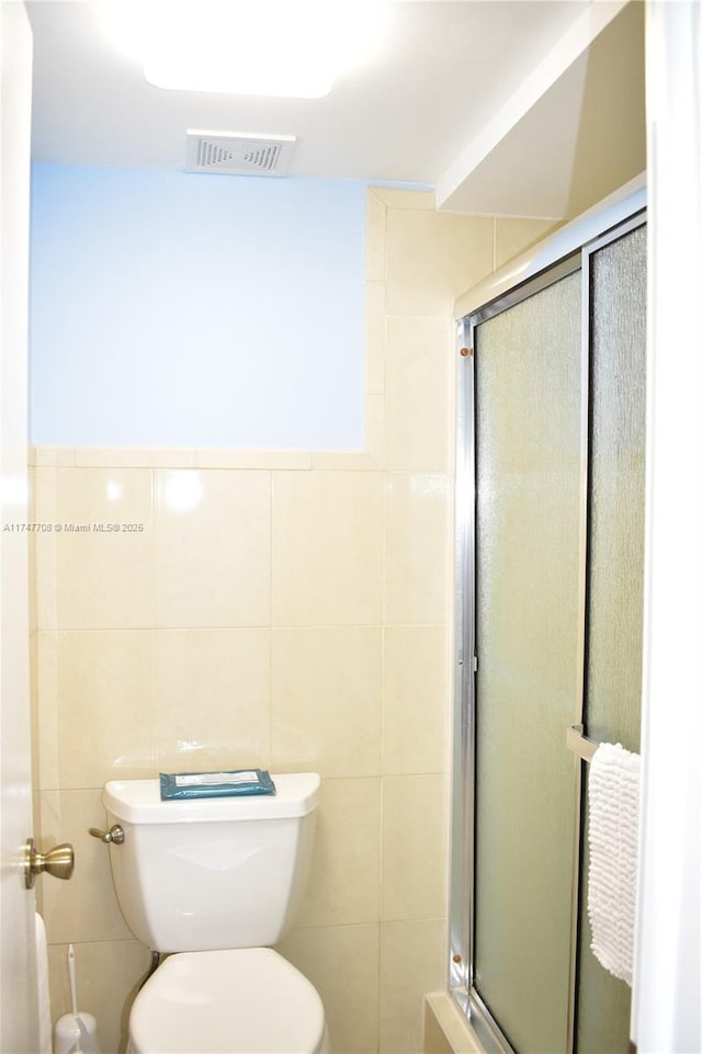 full bath with toilet, a shower stall, visible vents, and tile walls