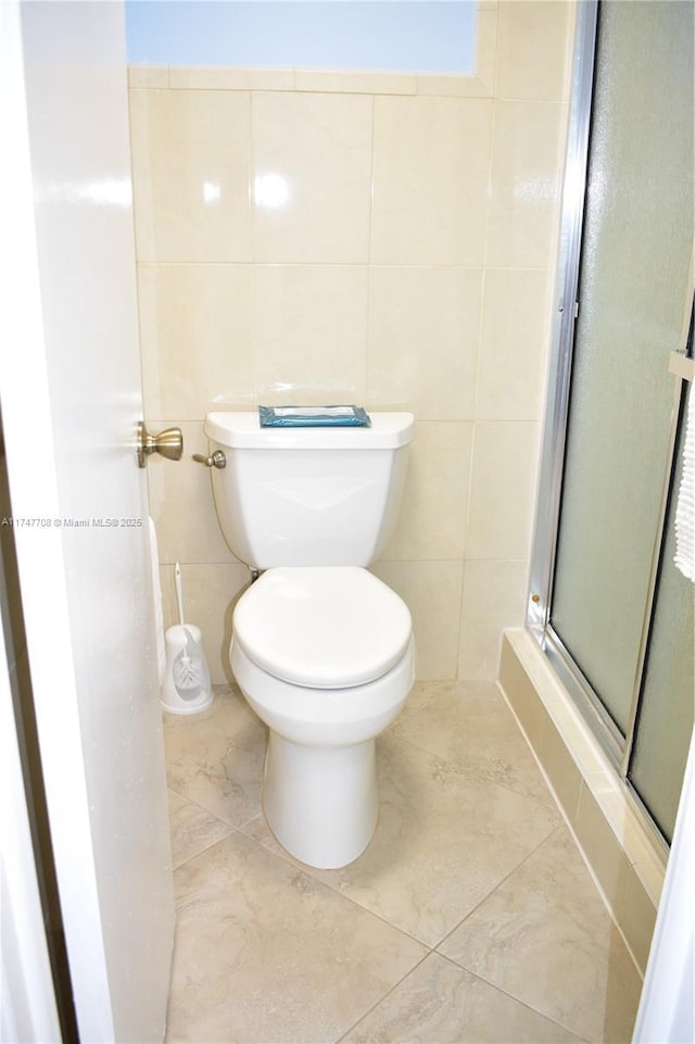 full bathroom featuring toilet, a shower stall, and tile walls