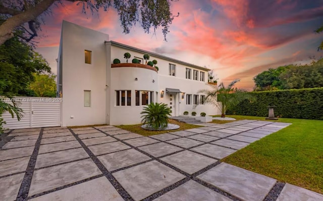 back house at dusk featuring a patio area and a lawn