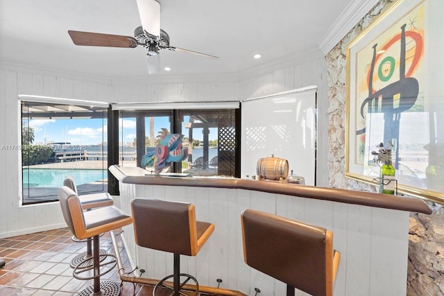 bar featuring ceiling fan, a water view, tile patterned floors, a bar, and crown molding