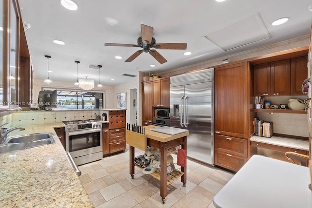 kitchen featuring brown cabinetry, light stone counters, appliances with stainless steel finishes, hanging light fixtures, and a sink