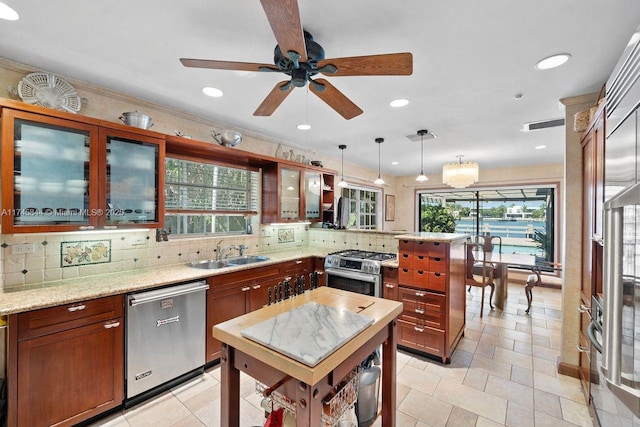 kitchen featuring stainless steel appliances, a sink, hanging light fixtures, light stone countertops, and glass insert cabinets