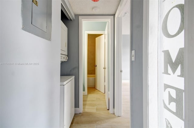 hallway with light wood-type flooring, electric panel, stacked washer and dryer, and a textured ceiling