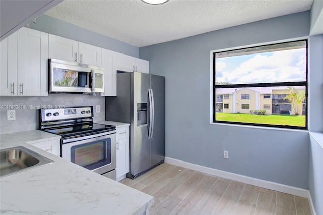 kitchen featuring tasteful backsplash, stainless steel appliances, light stone countertops, light wood-type flooring, and white cabinetry