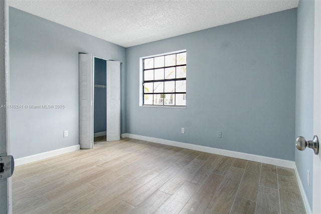 unfurnished bedroom featuring light hardwood / wood-style floors, a textured ceiling, and a closet