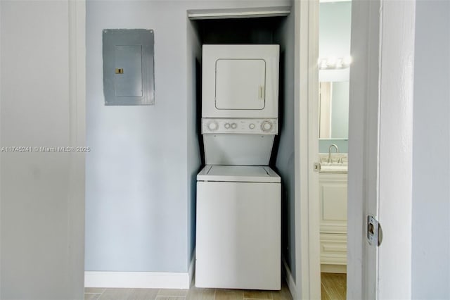 laundry area featuring electric panel, stacked washer and clothes dryer, and sink