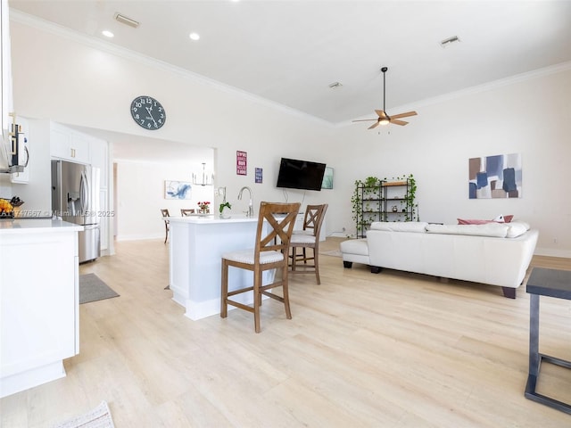 kitchen with light hardwood / wood-style floors, crown molding, stainless steel fridge, white cabinets, and a kitchen island with sink