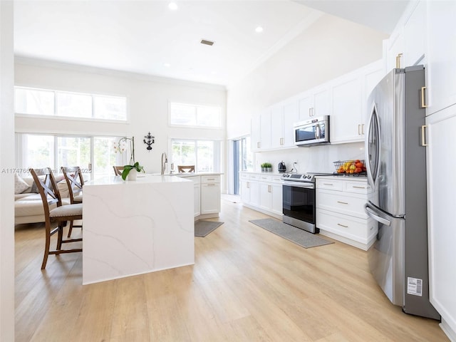 kitchen featuring appliances with stainless steel finishes, a breakfast bar, a kitchen island with sink, white cabinets, and a high ceiling