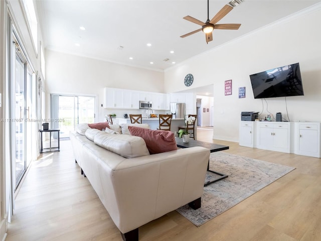 living room with ceiling fan, light hardwood / wood-style flooring, crown molding, and a towering ceiling