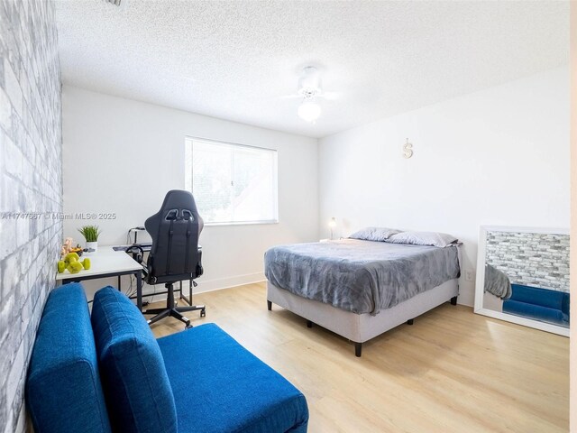 bedroom featuring a fireplace, ceiling fan, light hardwood / wood-style floors, and a textured ceiling