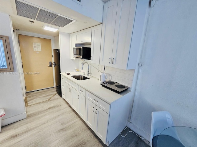 kitchen with sink, white cabinets, black refrigerator, and light hardwood / wood-style floors