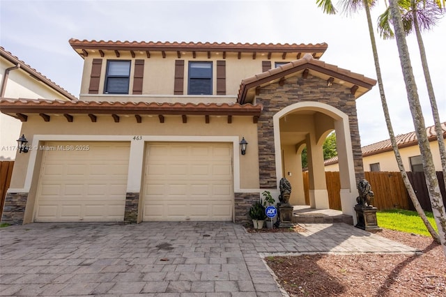 mediterranean / spanish house featuring decorative driveway, stucco siding, an attached garage, fence, and stone siding