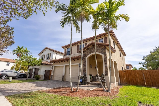 mediterranean / spanish home with decorative driveway, stone siding, fence, and stucco siding