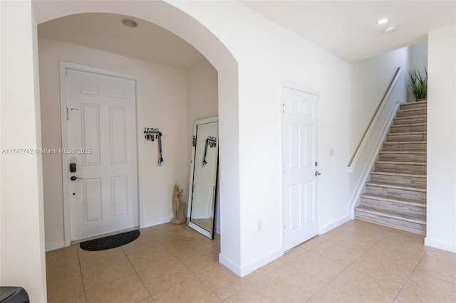 foyer entrance featuring arched walkways, stairway, light tile patterned flooring, and baseboards