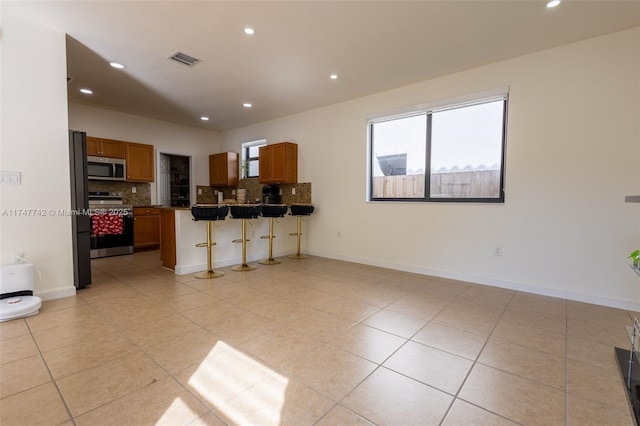 interior space featuring a breakfast bar area, open floor plan, appliances with stainless steel finishes, brown cabinets, and dark countertops