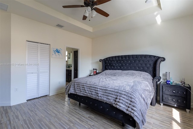 bedroom with visible vents, baseboards, ensuite bath, light wood-style flooring, and a tray ceiling