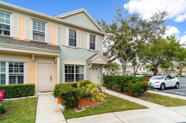 multi unit property with uncovered parking, a shingled roof, and stucco siding