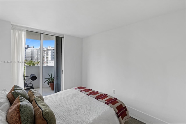 bedroom featuring access to exterior, a city view, floor to ceiling windows, and baseboards