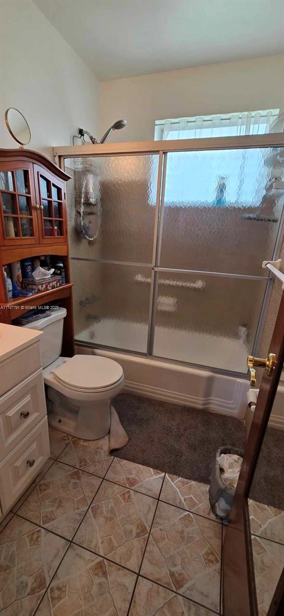 full bathroom featuring tile patterned floors, vanity, shower / bath combination with glass door, and toilet