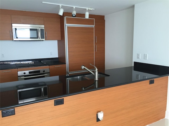 50 Biscayne Blvd Unit 3505, Miami, FL 33132 - kitchen with stainless steel appliances, rail lighting, a sink, dark countertops, and brown cabinetry