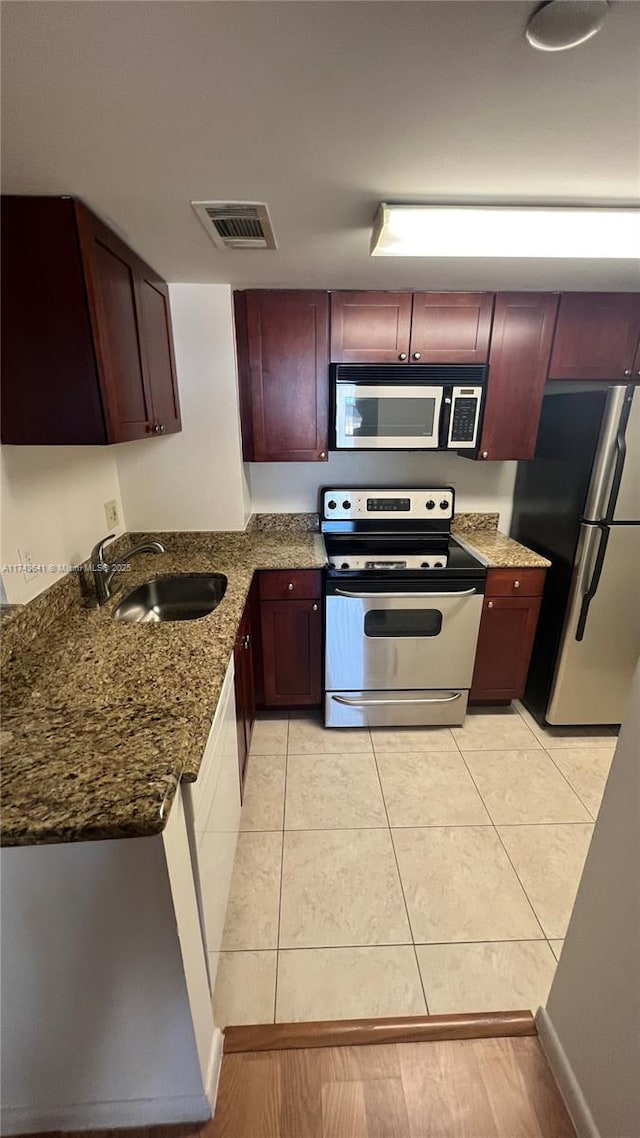 kitchen with dark stone countertops, visible vents, light tile patterned floors, a sink, and appliances with stainless steel finishes