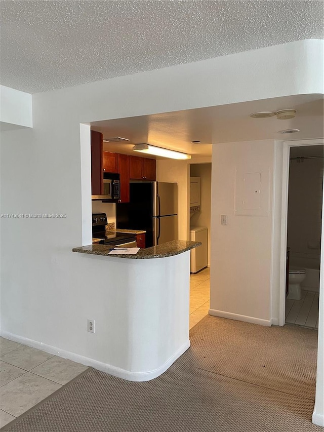 kitchen featuring dark stone countertops, baseboards, a peninsula, a textured ceiling, and stainless steel appliances