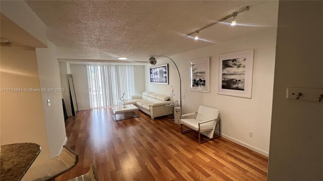 living room featuring track lighting, baseboards, wood finished floors, and a textured ceiling