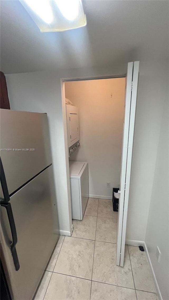 washroom featuring stacked washer / dryer, laundry area, light tile patterned flooring, and baseboards