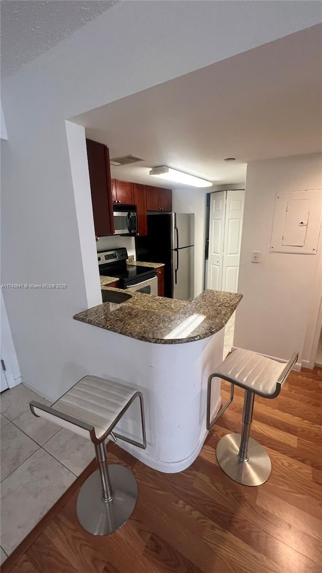 kitchen with a kitchen breakfast bar, electric panel, a peninsula, light wood-style flooring, and stainless steel appliances