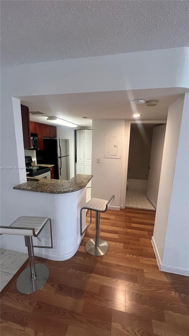 kitchen with light wood-type flooring, electric range oven, a kitchen bar, and a textured ceiling