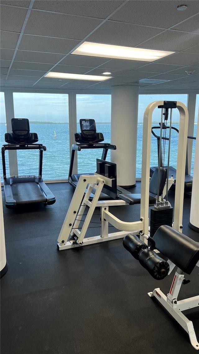 workout area featuring a water view, a paneled ceiling, and a wall of windows