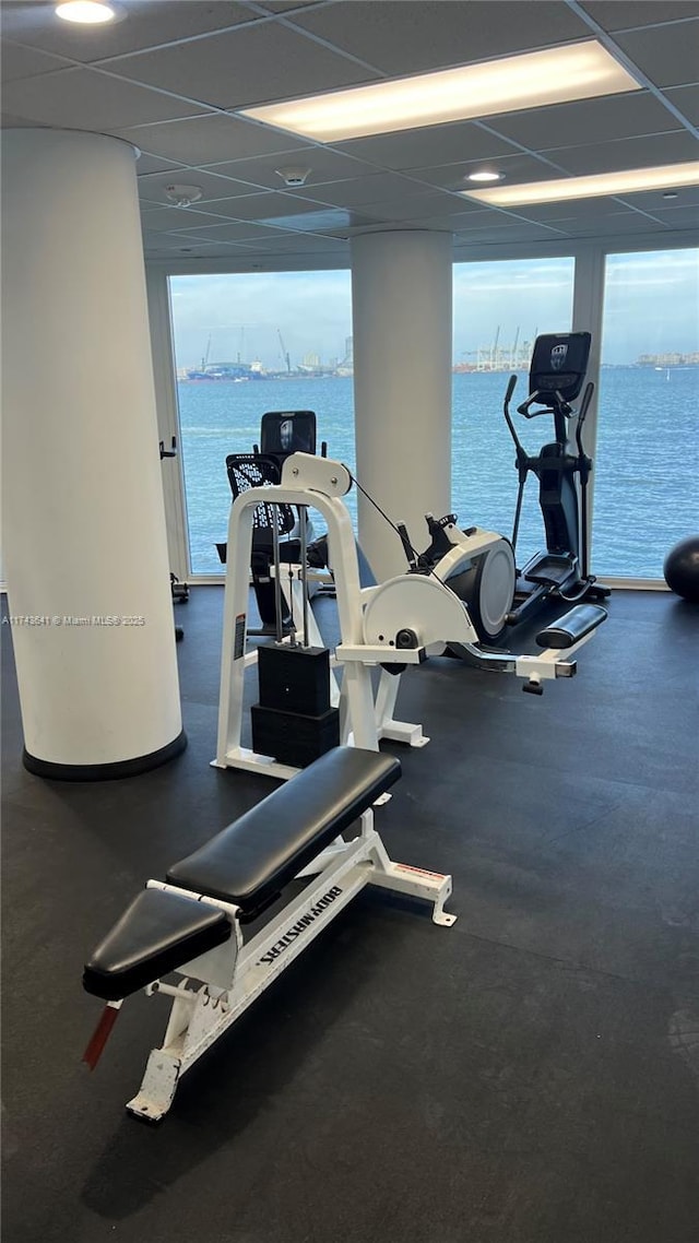 gym featuring a water view, a paneled ceiling, and a healthy amount of sunlight