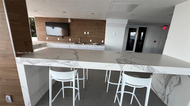 kitchen with light stone counters, wood walls, a sink, and a kitchen breakfast bar