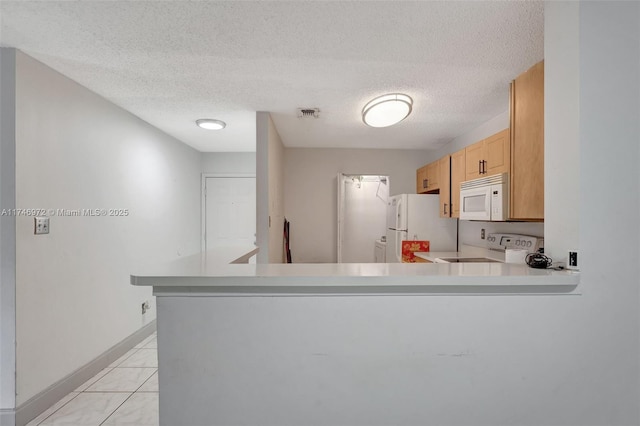 kitchen with white appliances, light tile patterned floors, a textured ceiling, light brown cabinets, and kitchen peninsula