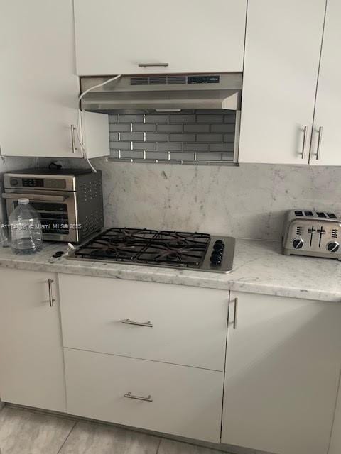 kitchen featuring white cabinetry, stainless steel gas cooktop, backsplash, and light stone counters