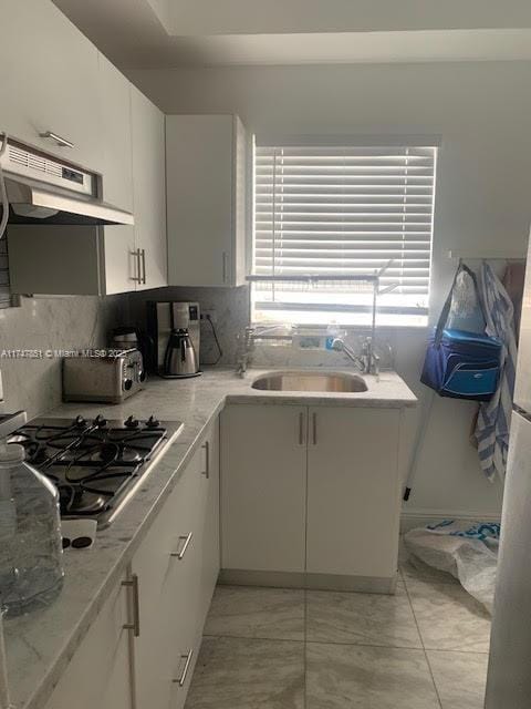 kitchen featuring sink, stainless steel gas cooktop, white cabinets, and tasteful backsplash