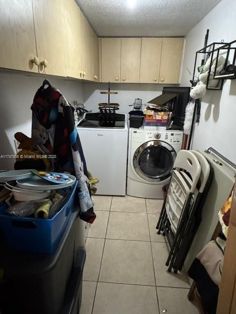 washroom with light tile patterned flooring, cabinets, a textured ceiling, and independent washer and dryer