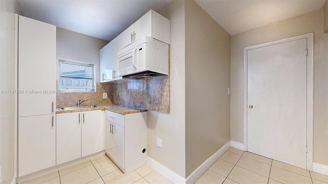 kitchen with light tile patterned flooring, white cabinetry, sink, and backsplash