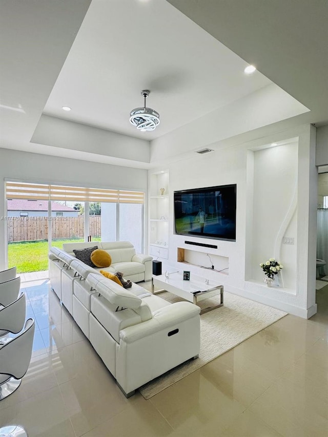 tiled living room with built in shelves, a wealth of natural light, and a raised ceiling