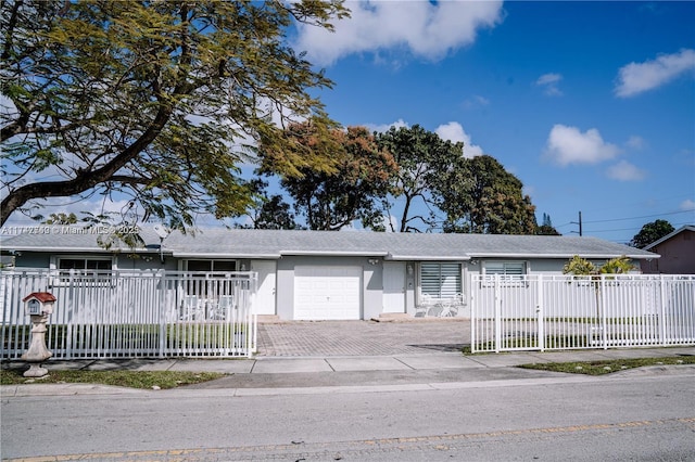 ranch-style home featuring an attached garage, a fenced front yard, decorative driveway, and stucco siding