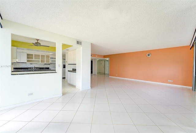 unfurnished living room featuring ceiling fan, light tile patterned floors, and a textured ceiling