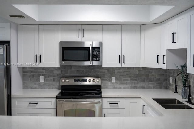 kitchen with tasteful backsplash, light countertops, appliances with stainless steel finishes, white cabinetry, and a sink