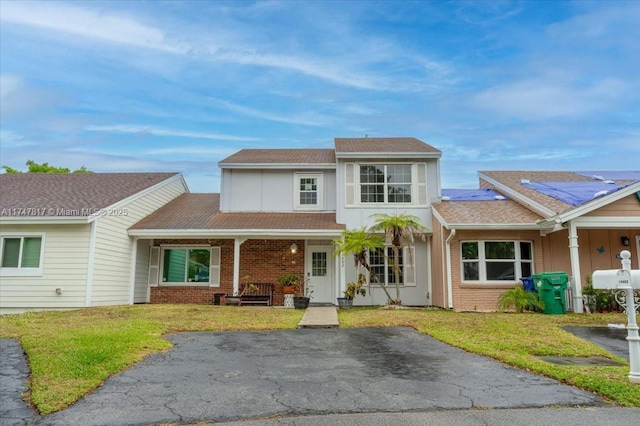 view of front facade with a porch, brick siding, a front lawn, and roof with shingles